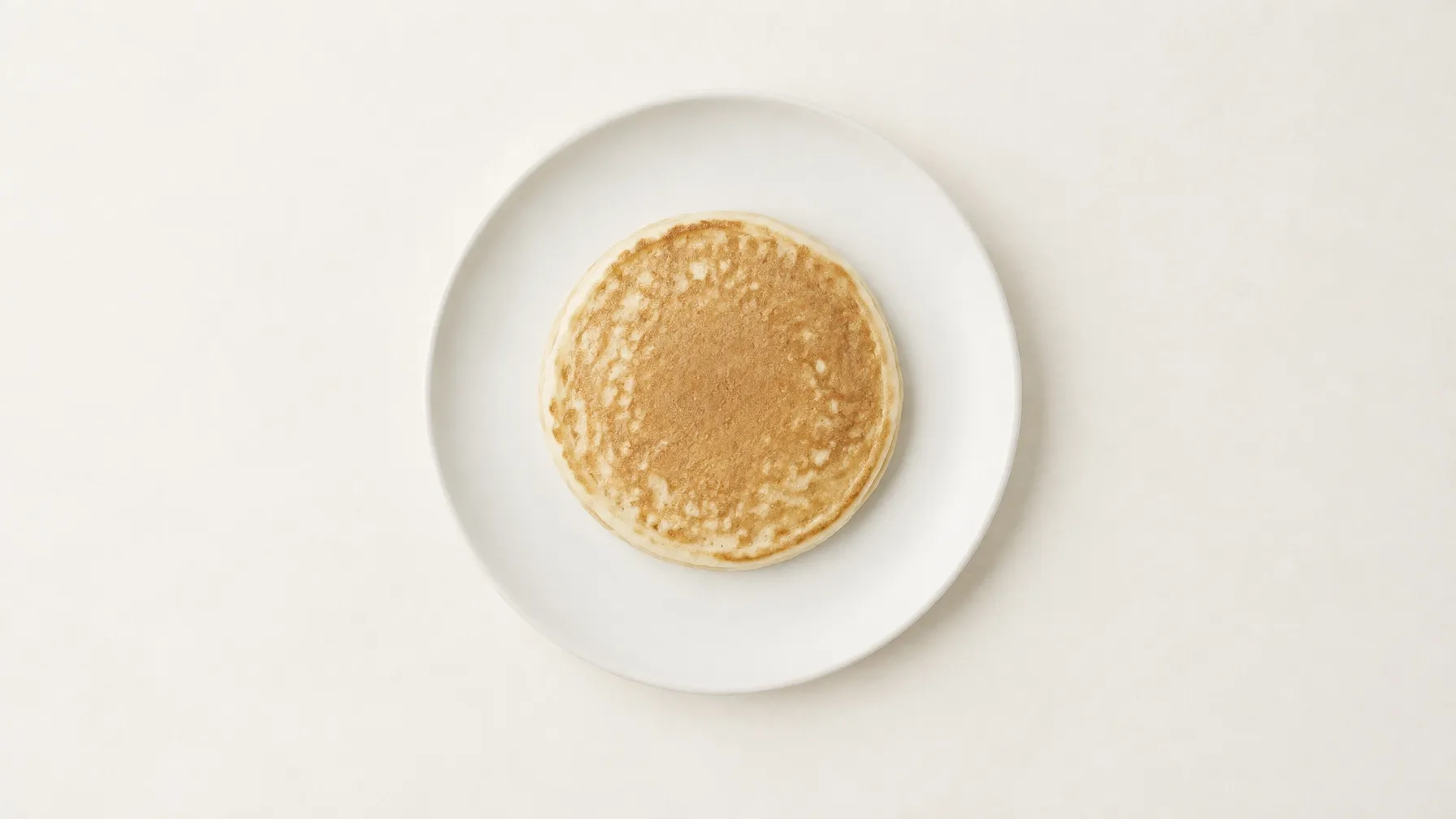 A single vanilla pancake on a plain ceramic plate